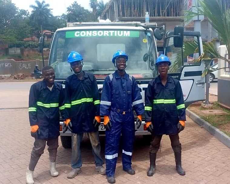 Four crew members in overalls and helmets in front of a collection truck